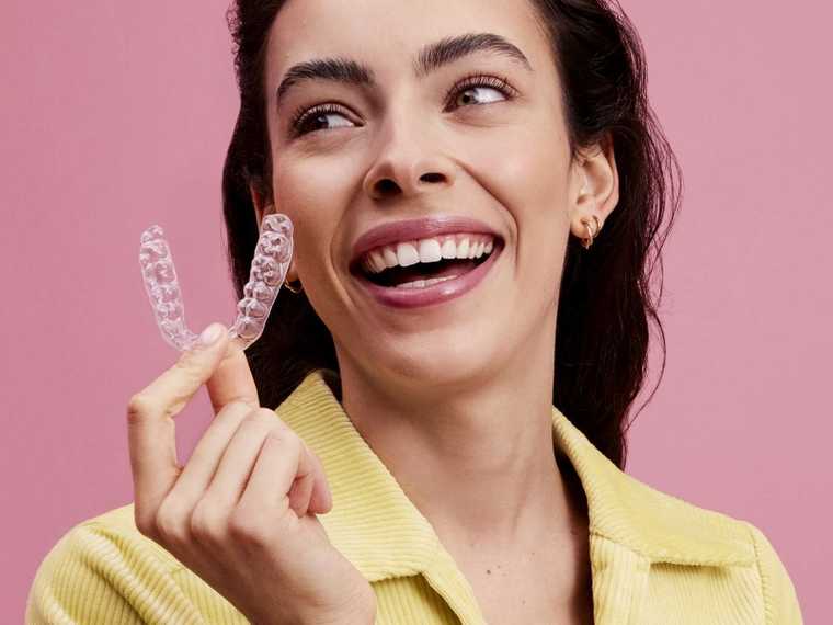 Mujer sonriente sujetando un aparato de ortodoncia invisible